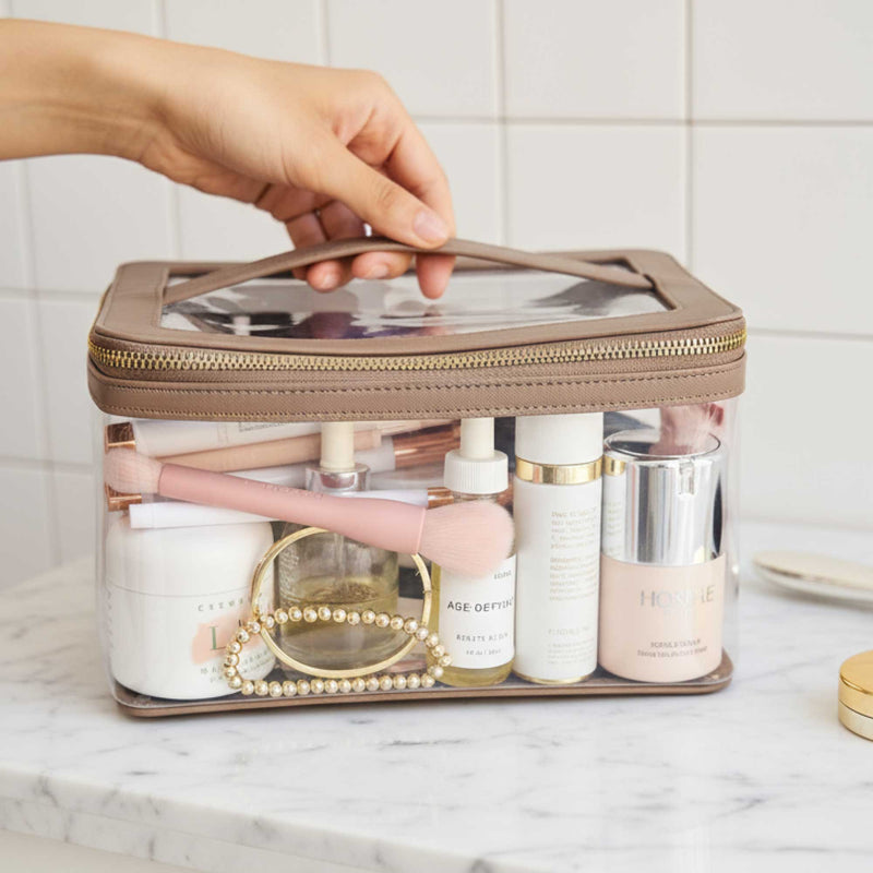 Truffle Clear Jumbo Train Case with Toffee leather trim containing beauty products on a marble surface.