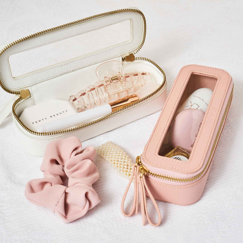 Truffle Mini Jetset Cases packed with beauty items on a white bedspread. 