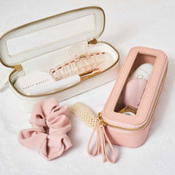 Truffle Mini Jetset Cases packed with beauty items on a white bedspread. 