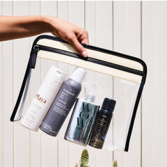 Clear Truffle Clarity Pouch Large filled with skincare and hair products on a light wooden background.
