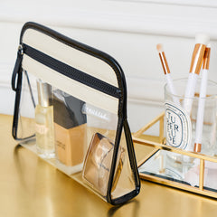 Clear Clarity Pouch Small, trimmed in natural colored nylon, filled with beauty items, sitting on a vanity.